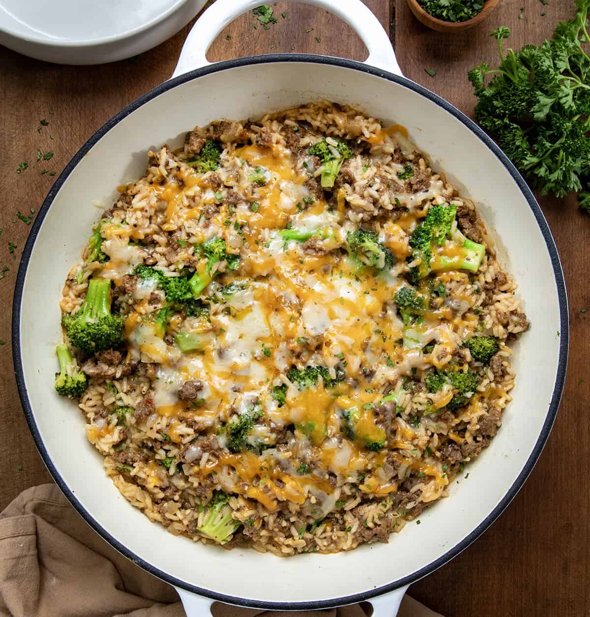 This Cheesy Beef Broccoli and Rice Skillet is the kind of one-pan dinner you can count on! It's hearty, comforting, and ready in about 30 minutes! Everything cooks in one skillet, from the seasoned ground beef to the tender rice and broccoli. Then it’s finished with two kinds of melty cheddar cheese for a dinner that is easy to make and even easier to love! I could gobble this up any time! Looking down on a skillet of Beef Broccoli and Rice Skillet on a wooden table.