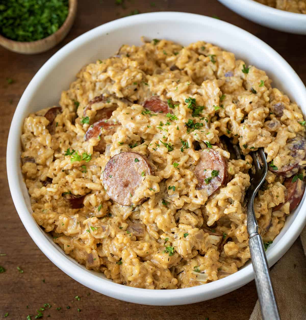 Bowl of Cajun Sausage and Rice with a fork in it on a wooden table.