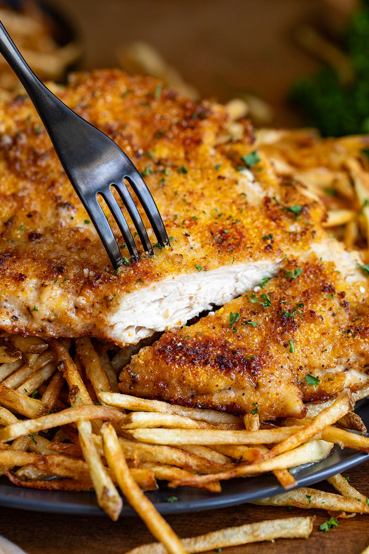 Sliced into piece of chicken that is resting on french fries.