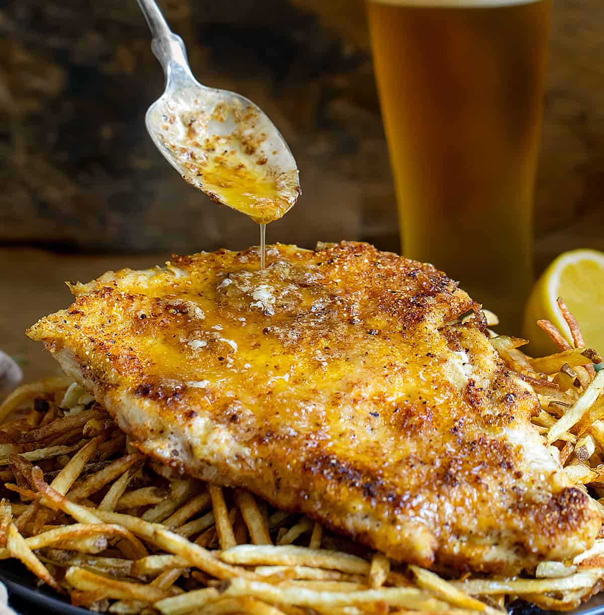 Spooning lemon butter sauce over crispy chicken resting on a plate of fries.
