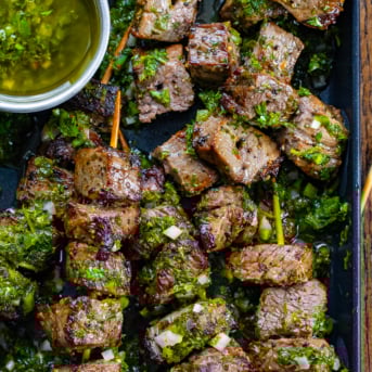 Chimichurri Steak Skewers in a pan on a wooden table from overhead.