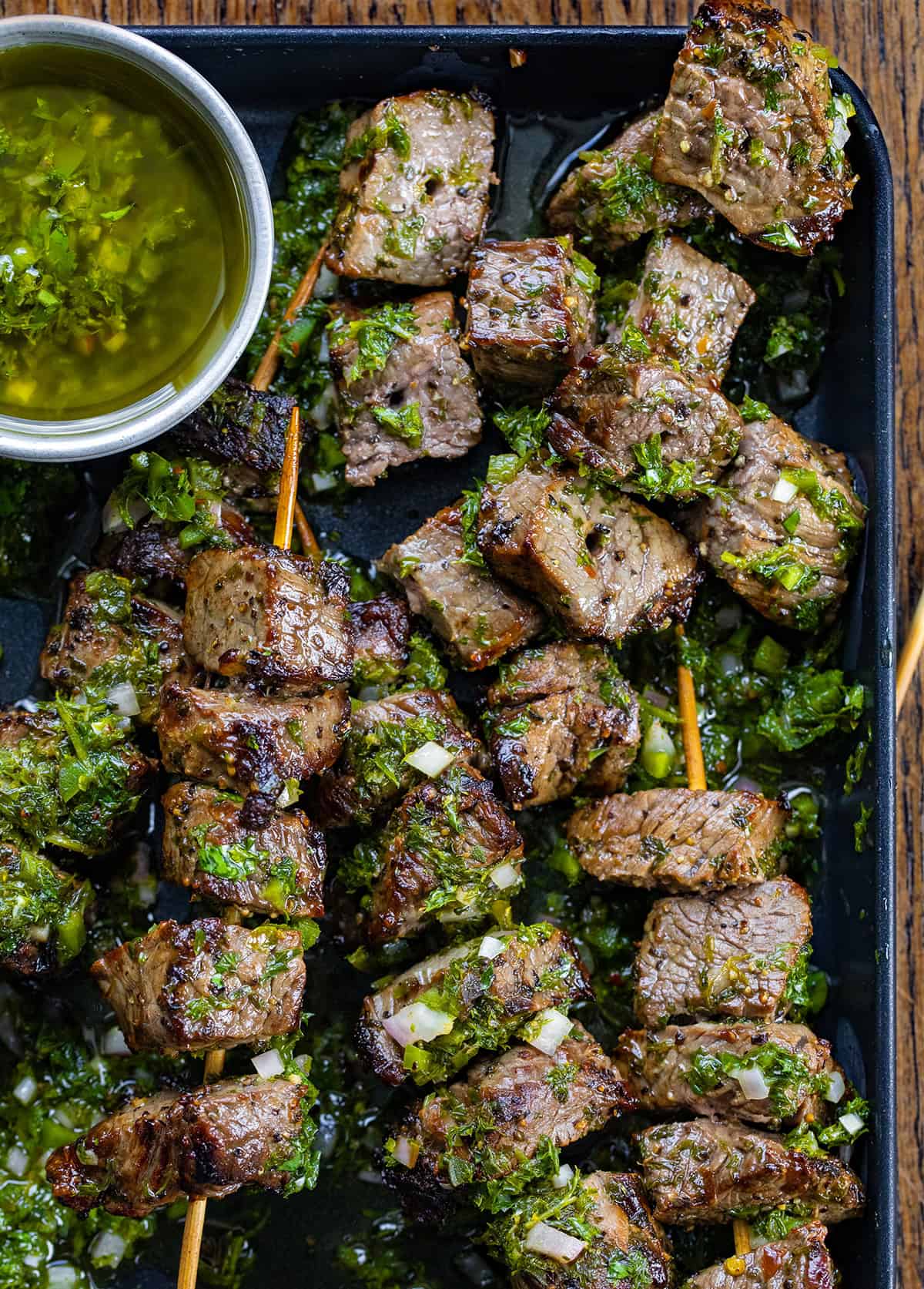 Chimichurri Steak Skewers in a pan on a wooden table from overhead.