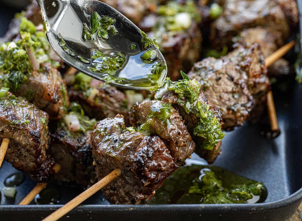 Drizzling Chimichurri sauce over steak bites very close up.