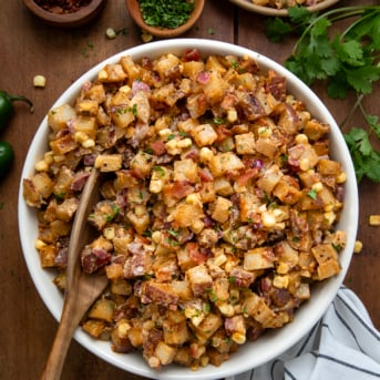 White bowl filled with Chipotle Roasted Potato Salad with a spoon in it on a wooden table.