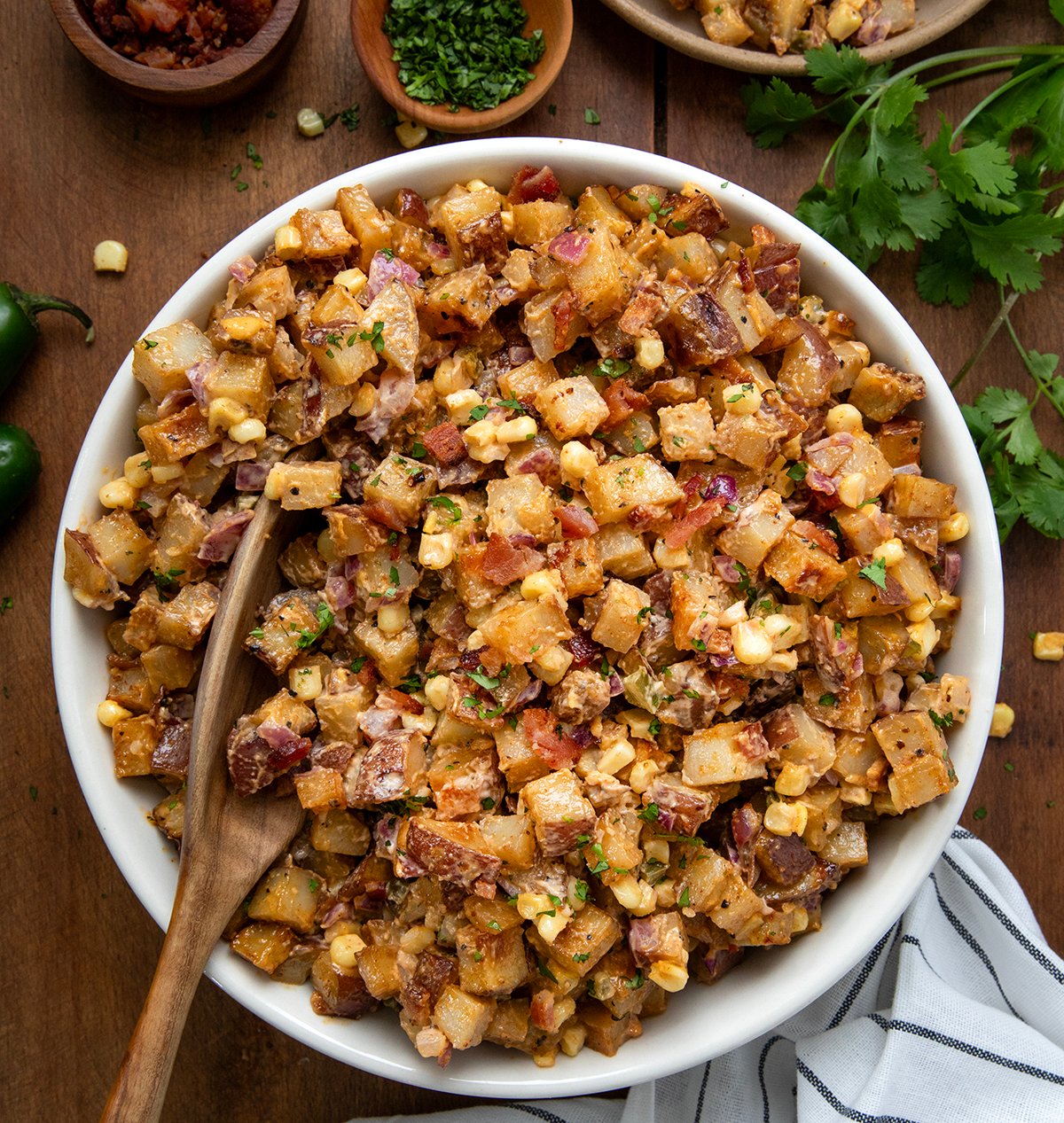 White bowl filled with Chipotle Roasted Potato Salad with a spoon in it on a wooden table.