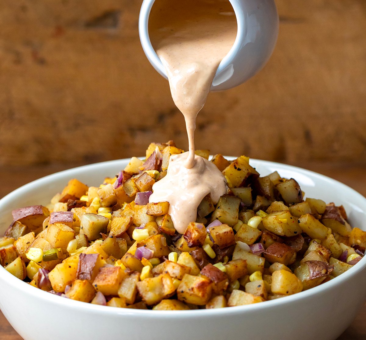 Pouring sauce over Chipotle Roasted Potato Salad.