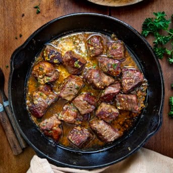 Skillet of Cowboy Butter Steak Bites on a wooden table from overhead.