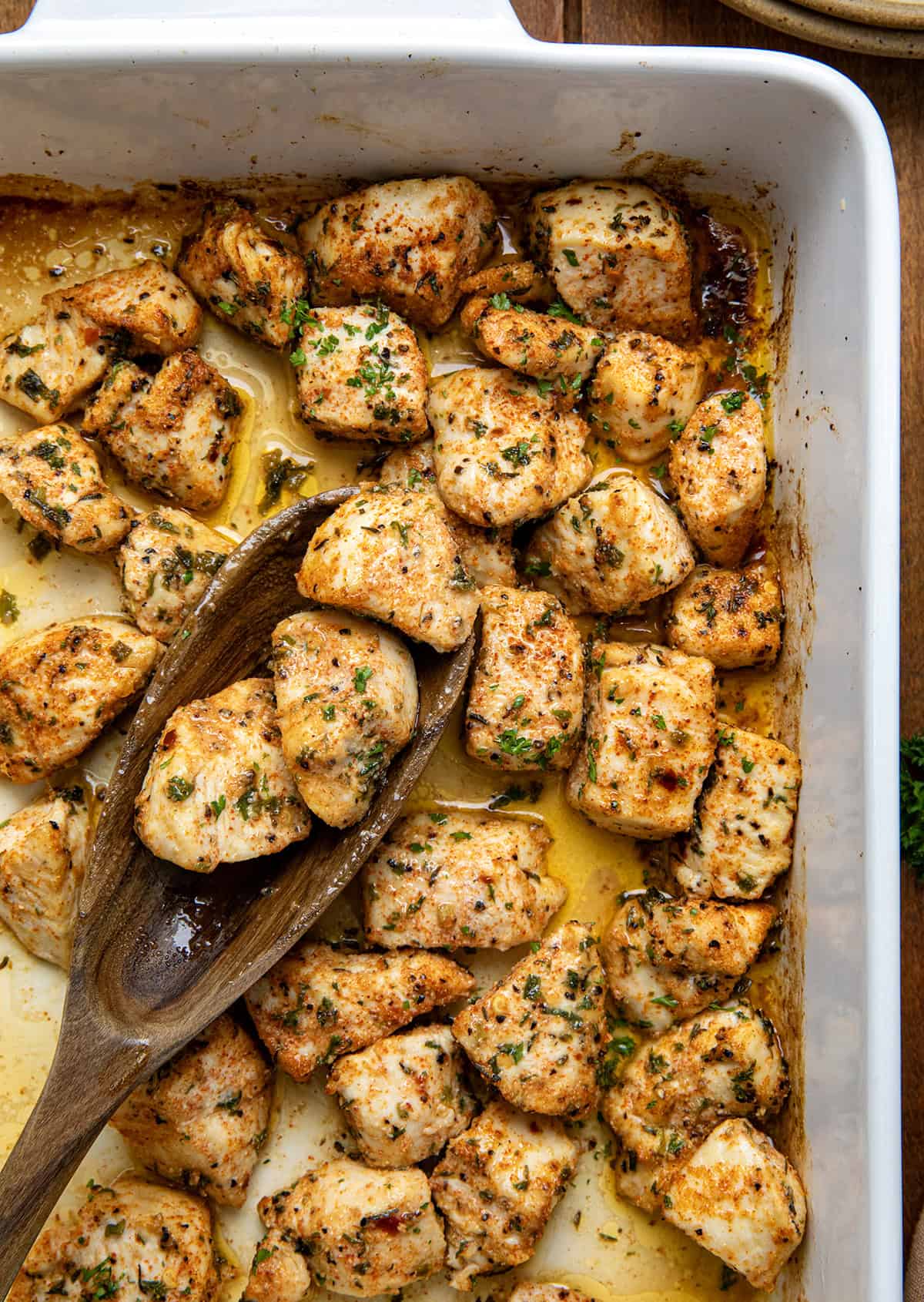 Cowboy Chicken Bites are bold, buttery, and oven-baked to perfection. Juicy chunks of chicken breast are tossed with smoky spices and drizzled with olive oil, then baked with cubed butter for a rich, flavorful finish. You can also make it in an air fryer! Casserole pan full of Cowboy Chicken Bites with a spoon in the pan shot from overhead.