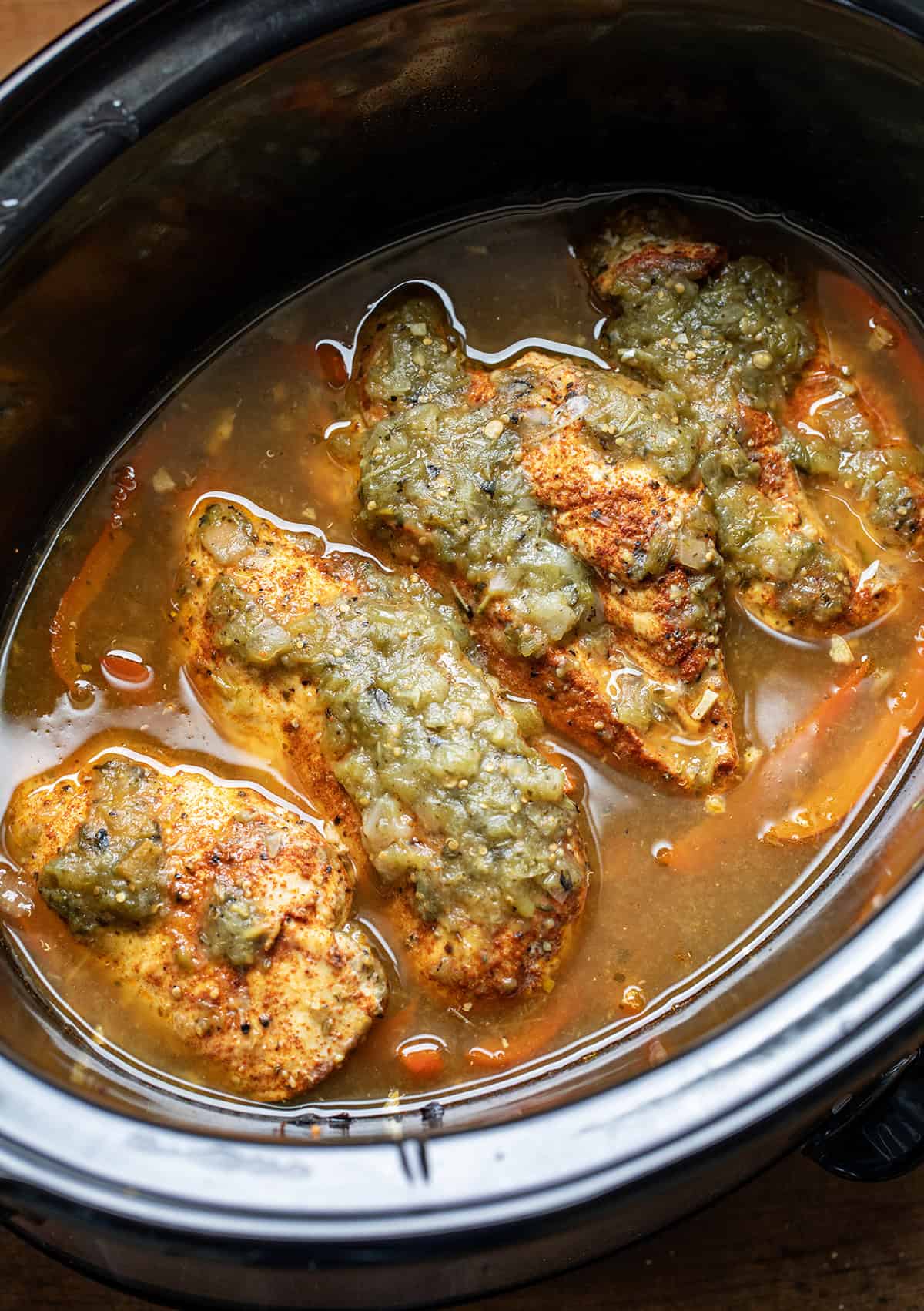 Chicken breasts in a crockpot with salsa verde before being shredded.