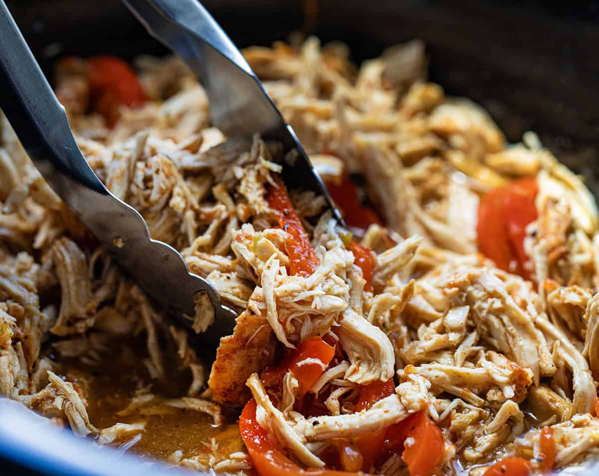 Using a tongs to pick up Crockpot Salsa Verde Chicken.