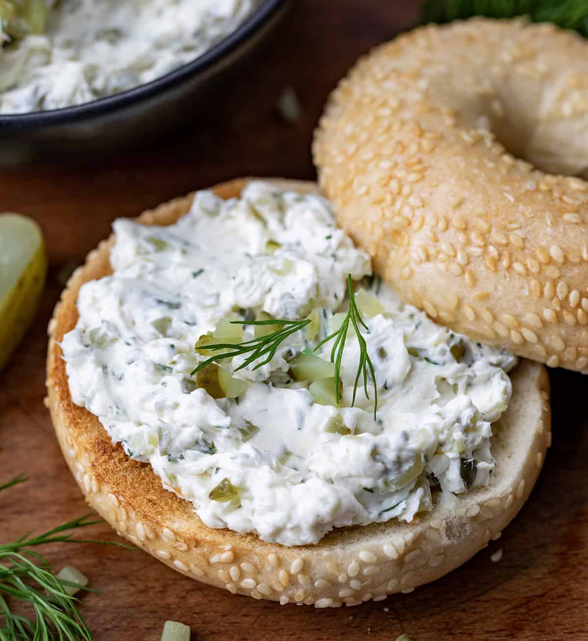 Bagel with Dill Pickle Cream Cheese spread on it on a wooden table.