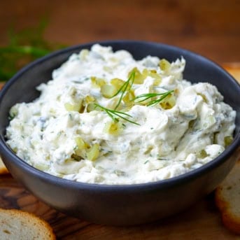 Bowl of Dill Pickle Cream Cheese on a wooden table with bagel chips.