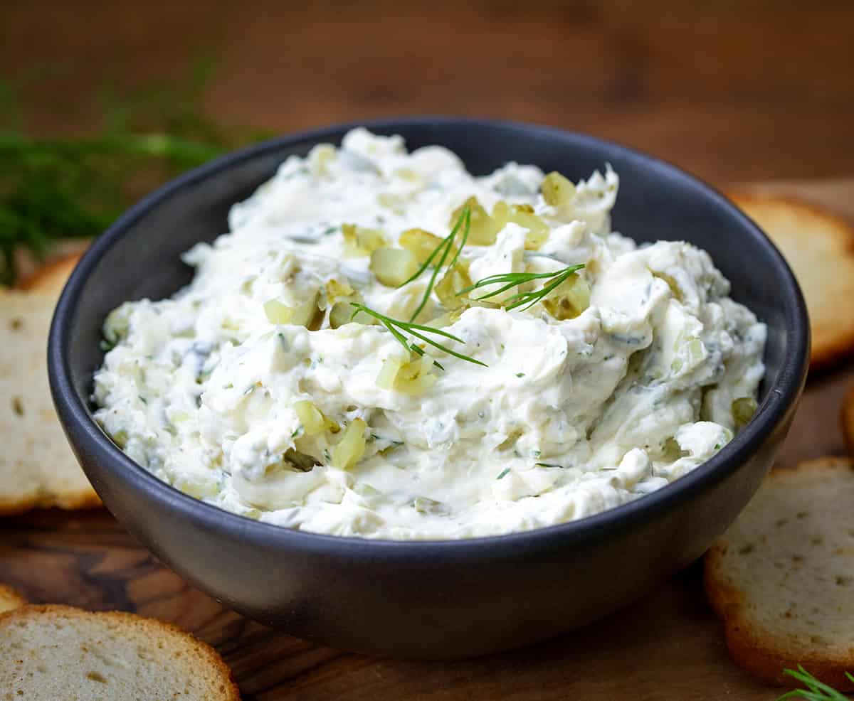 Bowl of Dill Pickle Cream Cheese on a wooden table with bagel chips.