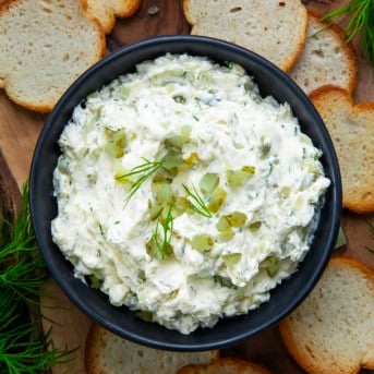 Bowl of Dill Pickle Cream Cheese on a wooden table with bagel chips all around.