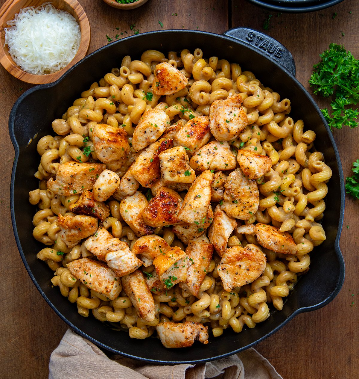 Skillet of Creamy Garlic Parmesan Chicken Pasta on a wooden table with fresh parmesan from overhead.