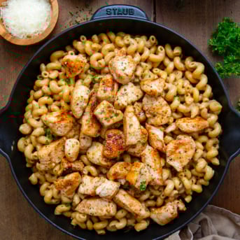 Skillet of Creamy Garlic Parmesan Chicken Pasta on a wooden table with fresh parmesan from overhead.