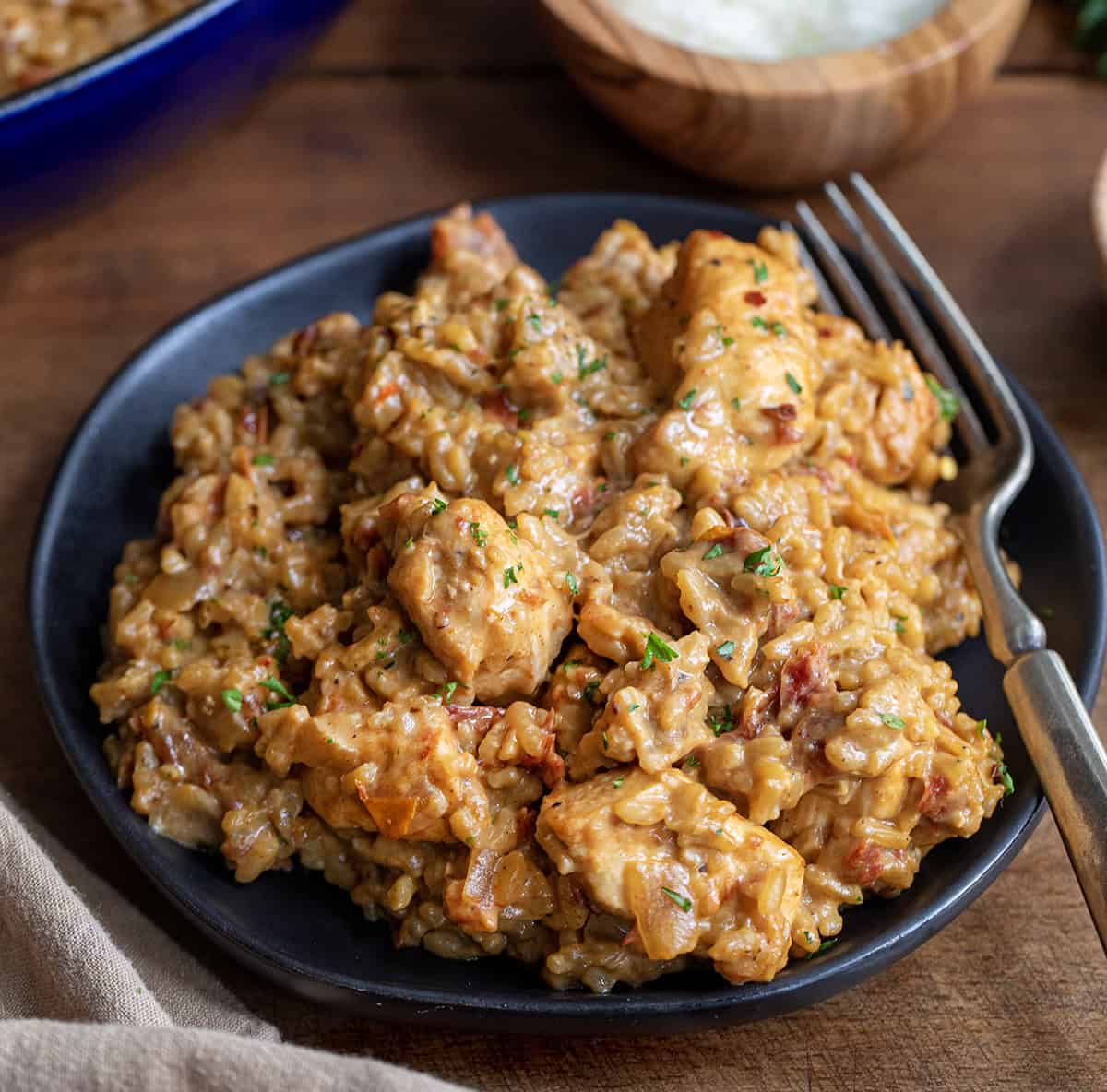 Black plate with Marry Me Chicken and Rice on it with a fork on a wooden table.
