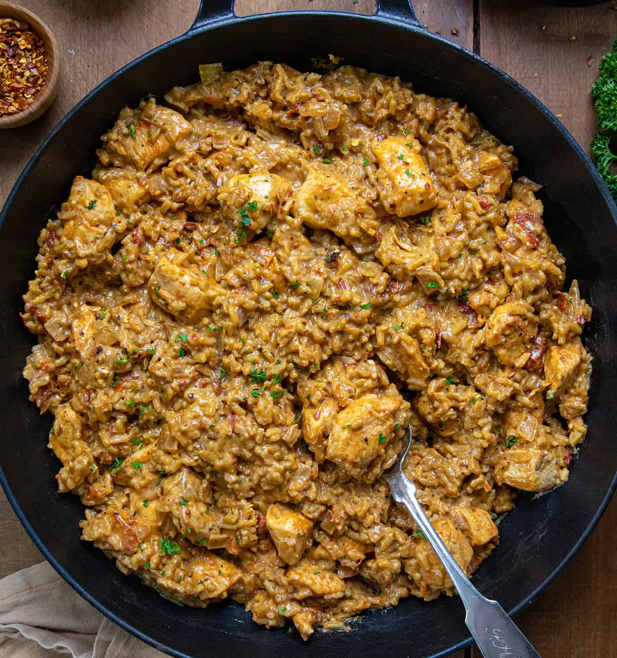 Skillet of Marry Me Chicken and Rice with a spoon in the pan on a wooden table from overhead.