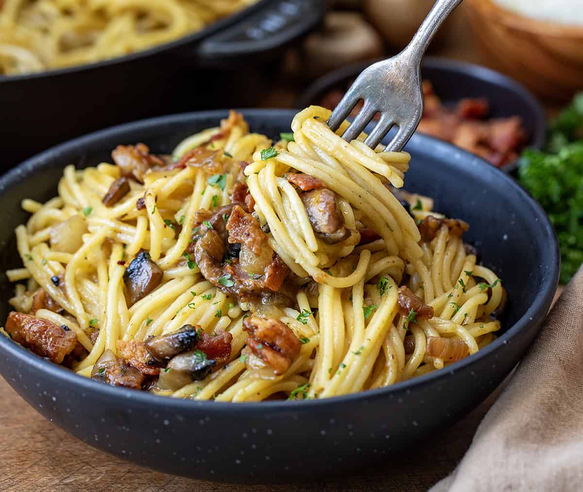 Fork swirling in Mushroom and Onion Carbonara in a black bowl.