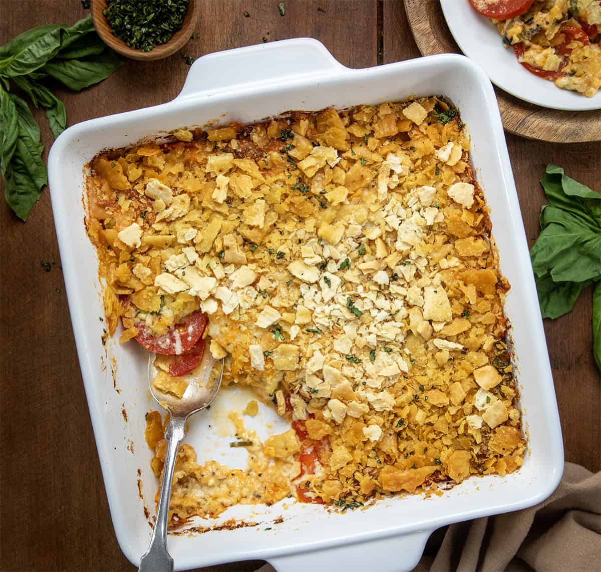 White pan of Scalloped Tomatoes with a potion missing and a spoon in the dish on a wooden table from overhead.