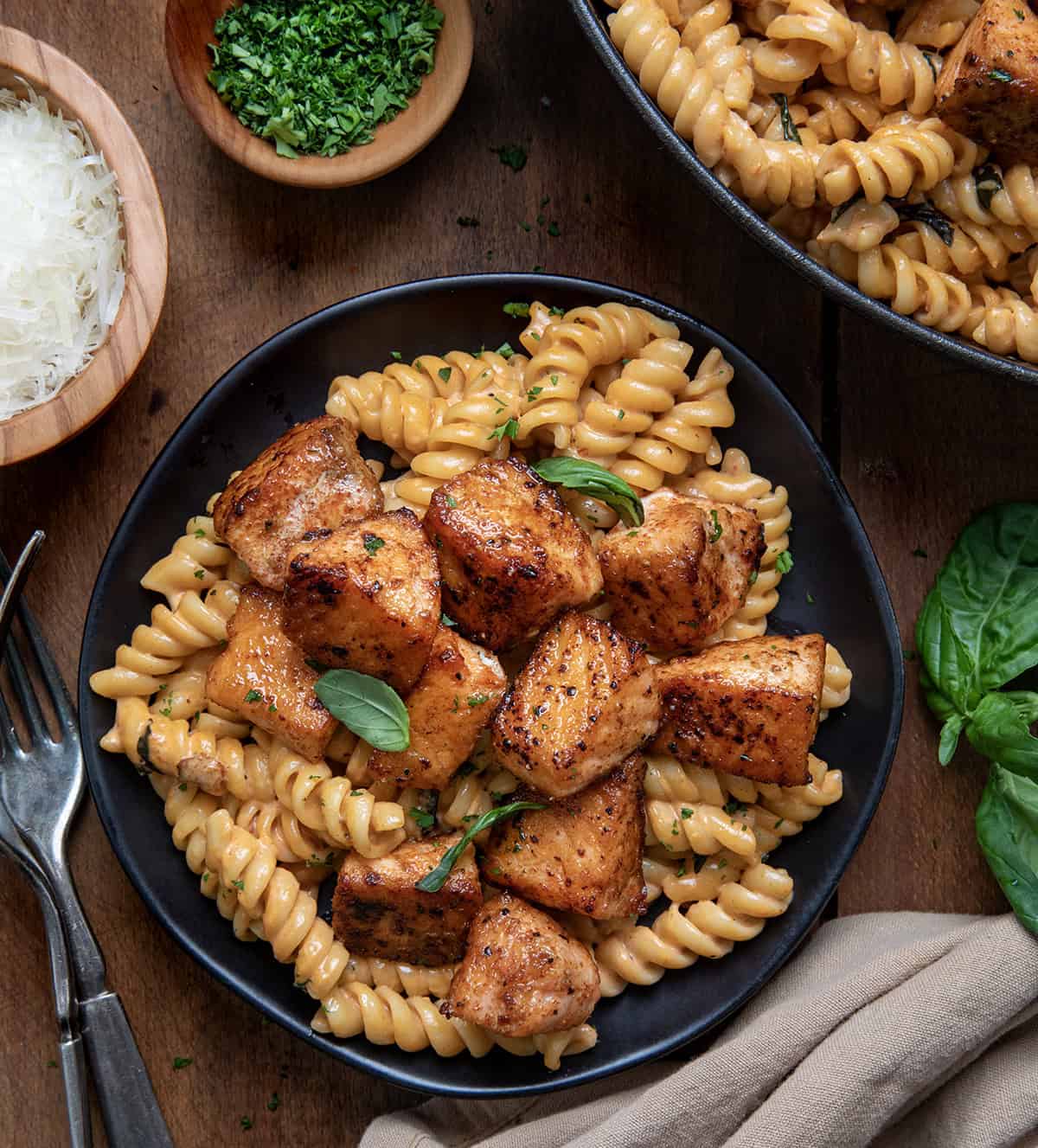Black plate with Tomato Basil Salmon Pasta on it next to a skillet on a wooden table.