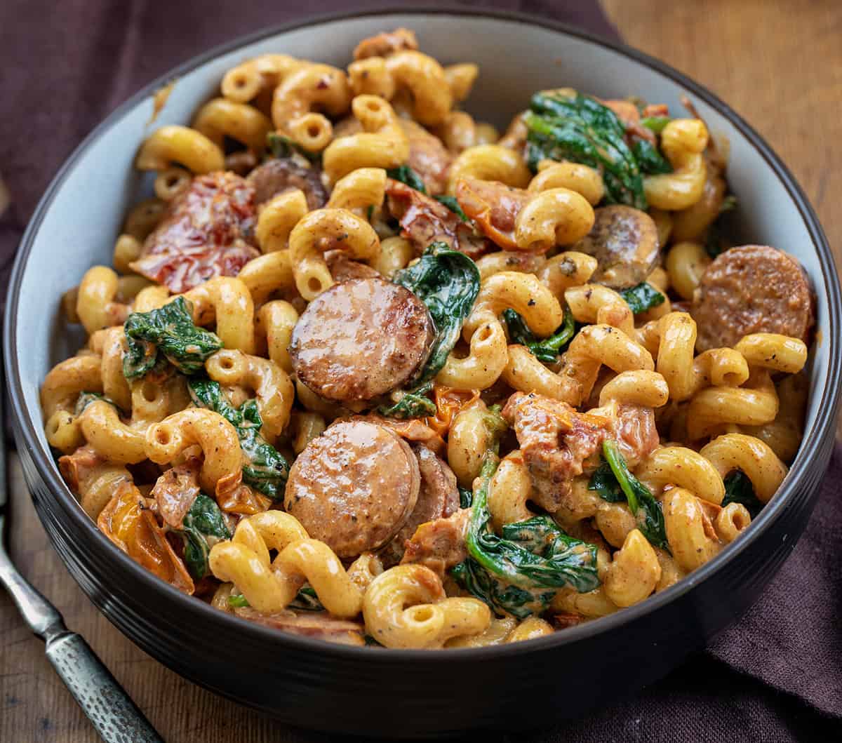 Bowl of Tuscan Sausage Pasta on a wooden table.