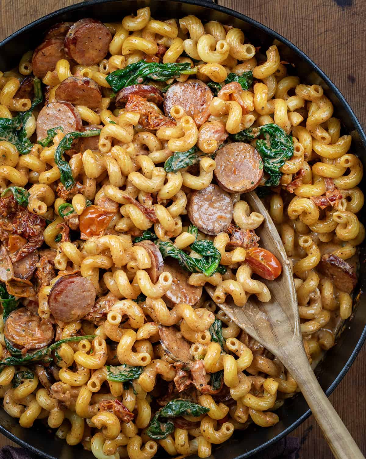 Skillet of Tuscan Sausage Pasta on a wooden table with a spoon in it close up.