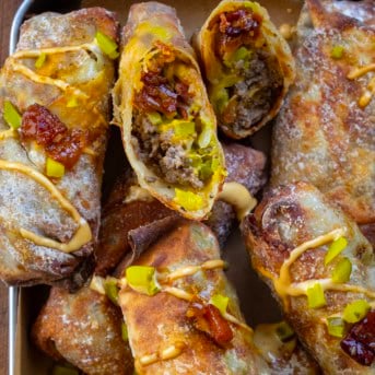 Bacon Jam Cheeseburger Egg Rolls in a tray and one is cut in half.