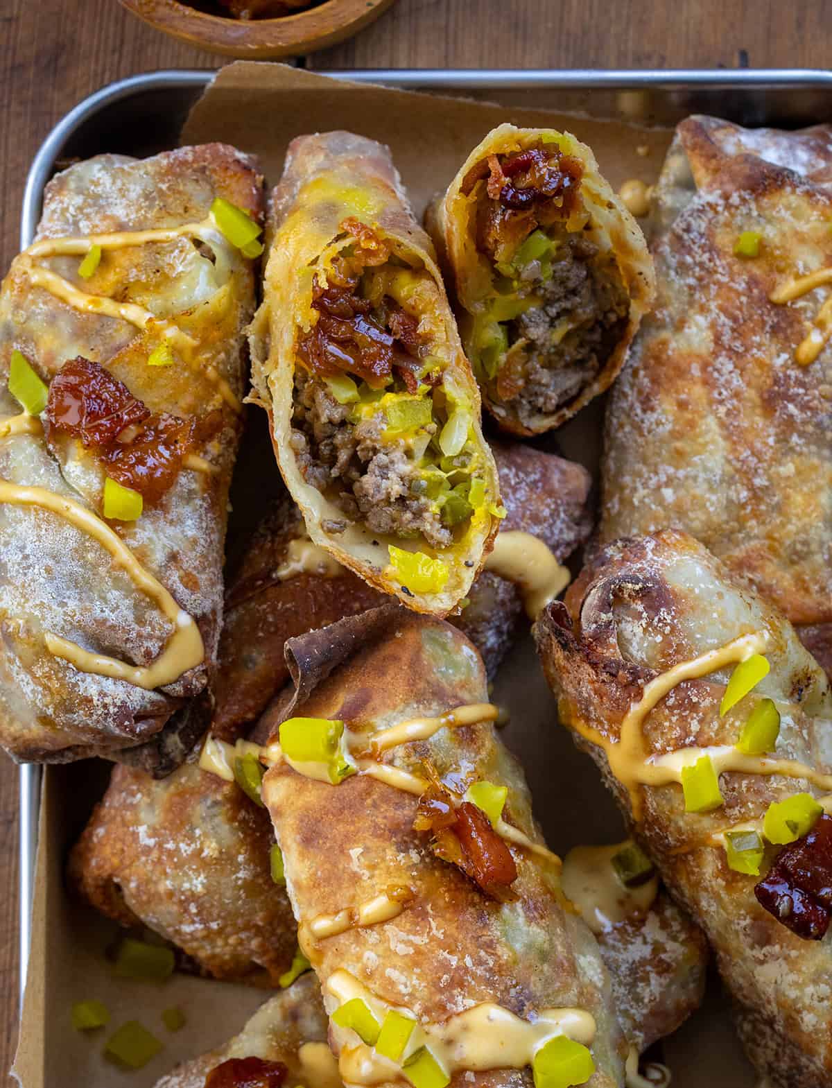 Bacon Jam Cheeseburger Egg Rolls in a tray and one is cut in half.
