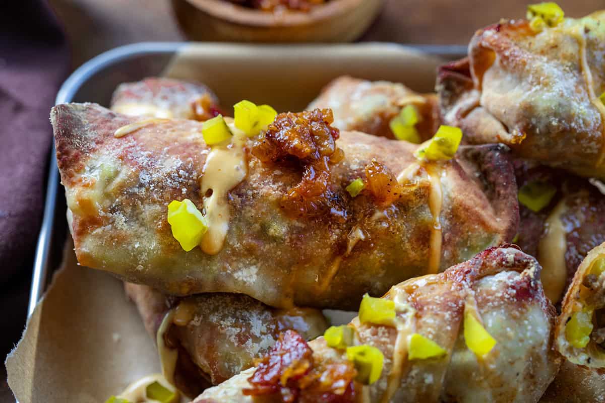 Close up of Bacon Jam Cheeseburger Egg Rolls covered in chopped pickles and bacon jam.