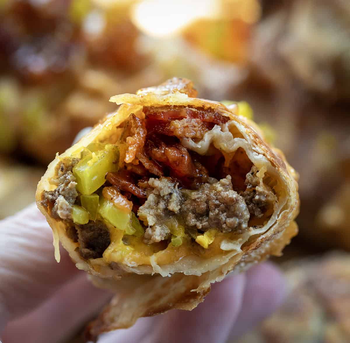 Bit into Bacon Jam Cheeseburger Egg Roll being held by a hand.