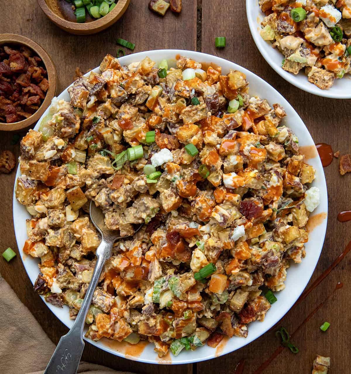 Buffalo Roasted Potato Salad is my popular (and simply the best!) Roasted Potato Salad with a bold, buffalo-flavored twist. It starts with crispy, seasoned roasted (never boiled!) potatoes. Drizzle with a little extra buffalo sauce or ranch, and you’ve got a flavorful side dish that’s anything but boring! Big bowl of Buffalo Roasted Potato Salad with a spoon in it on a wooden table from overhead.