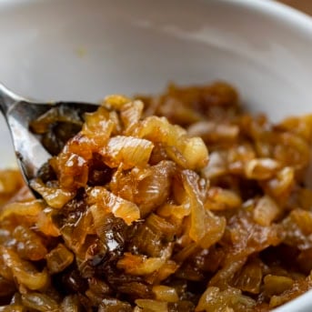 Spoonful of Caramelized Onions held above a white bowl of onions.