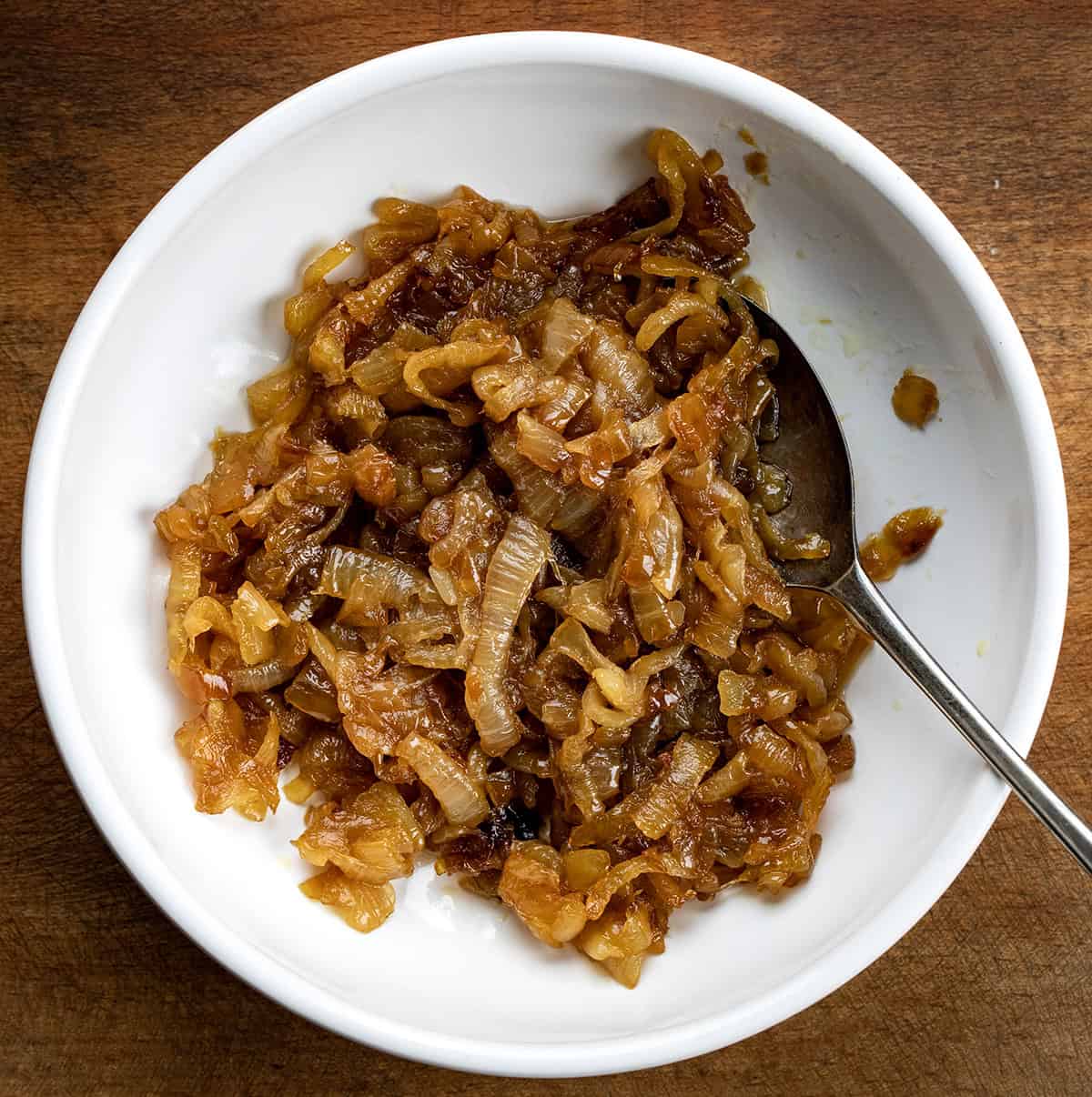 White bowl filled with Caramelized Onions on a wooden table from overhead.