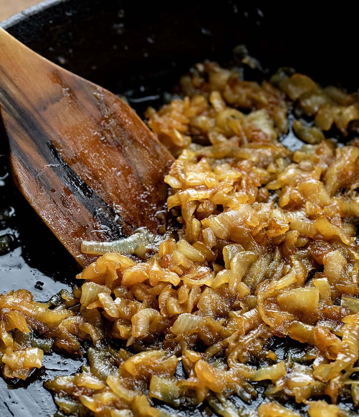 Caramelized Onions in a skillet with a wooden spoon close up.
