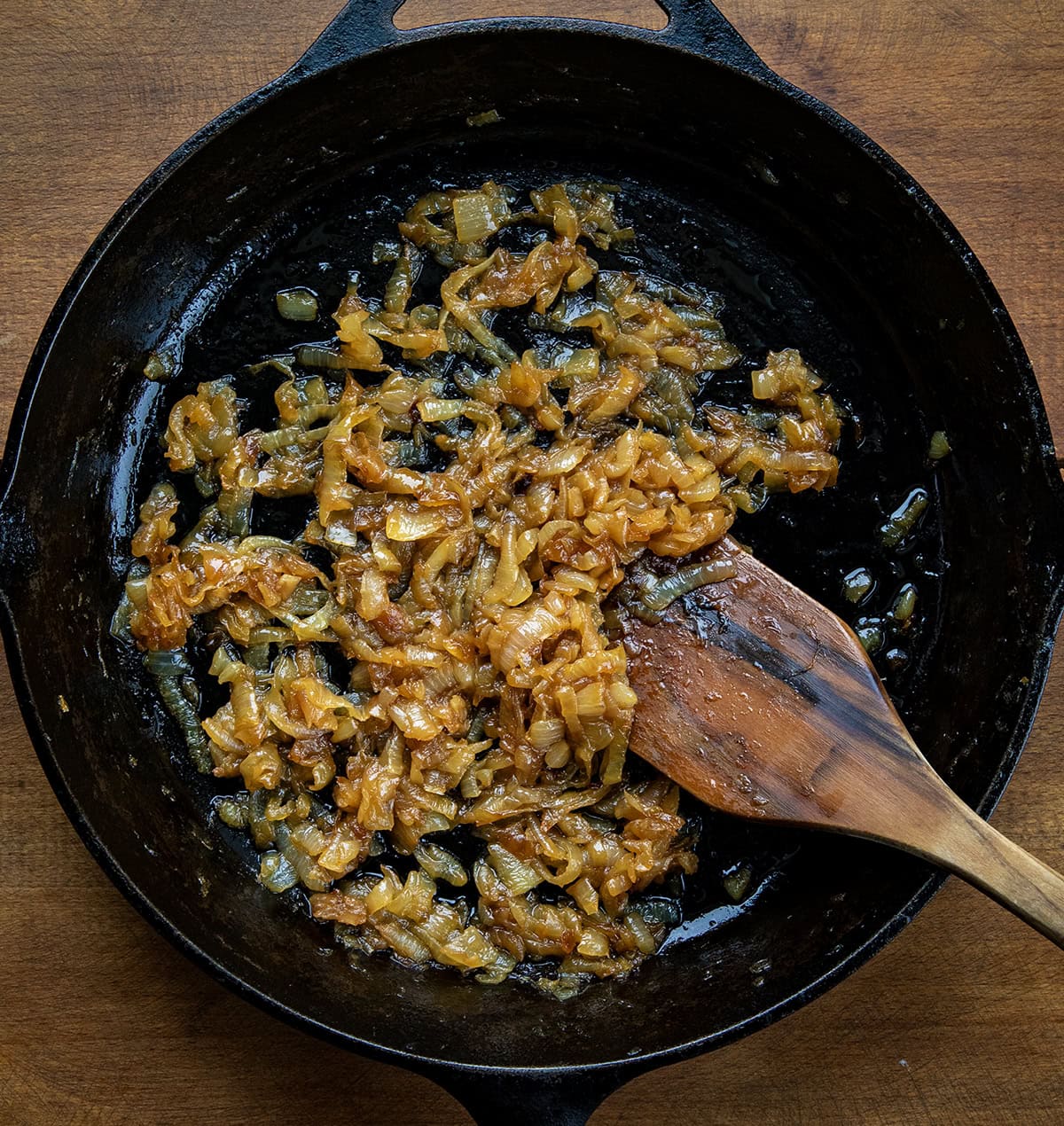 Skillet of Caramelized Onions on a wooden table with a wooden spoon from overhead.