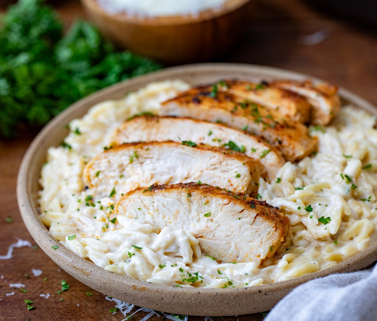 Slices chicken breast on top of a plate of alfredo orzo.
