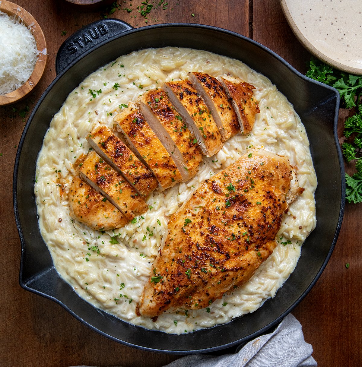 Chicken Alfredo Orzo in a skillet with one chicken breast cut into slices on a wooden table from overhead.