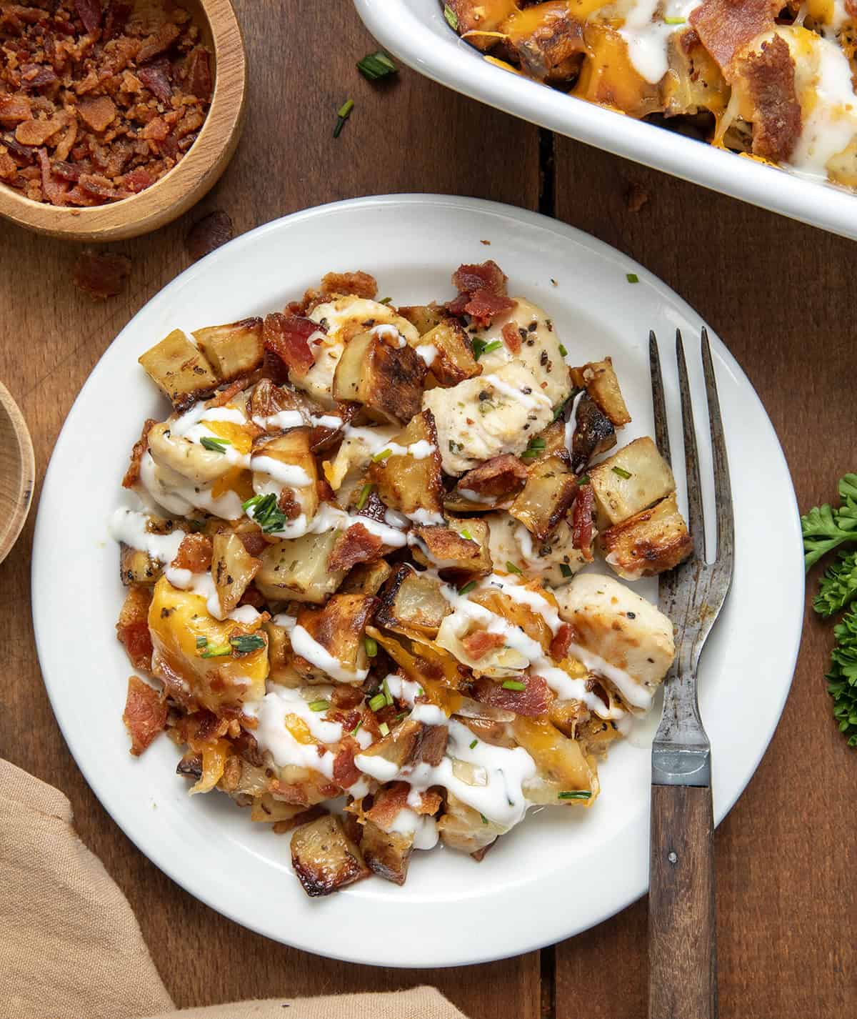 White plate with Chicken Bacon Ranch Roasted Potato Bake on it on a wooden table from overhead.