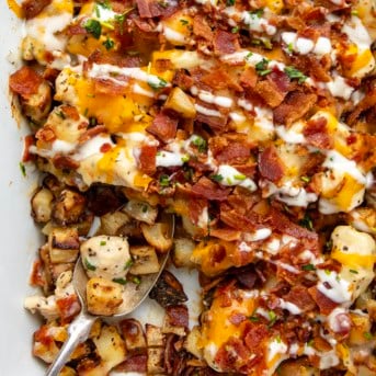 Close up of Chicken Bacon Ranch Roasted Potato Bake in a white casserole dish with a spoon.