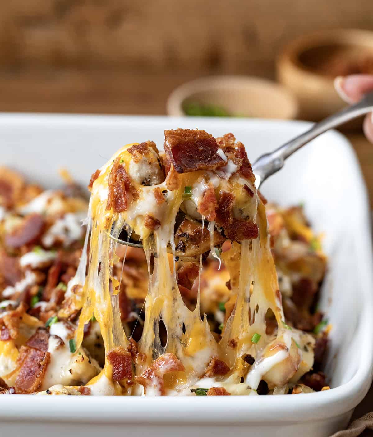 Spoon picking up a portion of Chicken Bacon Ranch Roasted Potato Bake with melty cheese pulling.