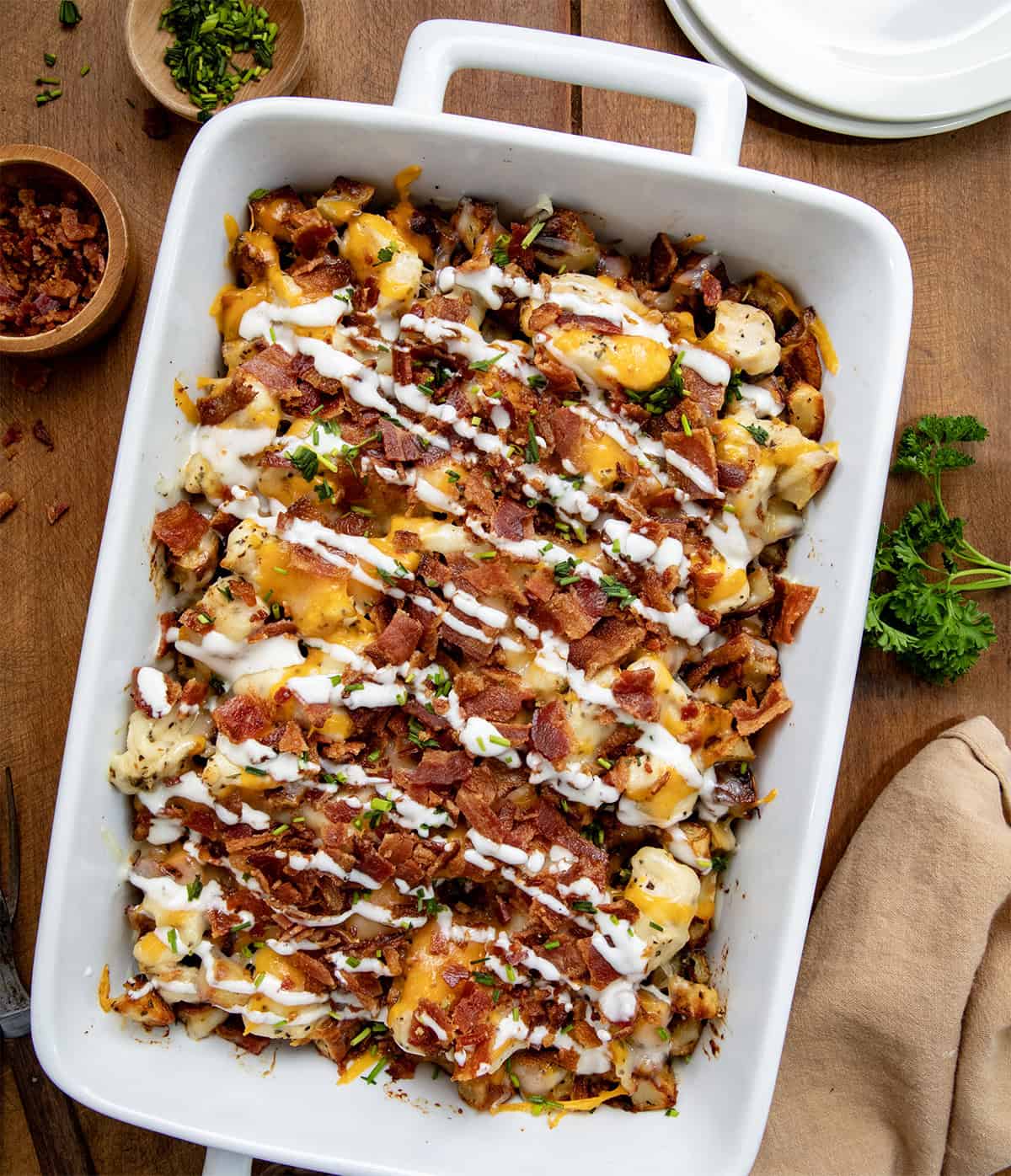 White casserole dish filled with Chicken Bacon Ranch Roasted Potato Bake on a wooden table from overhead. 