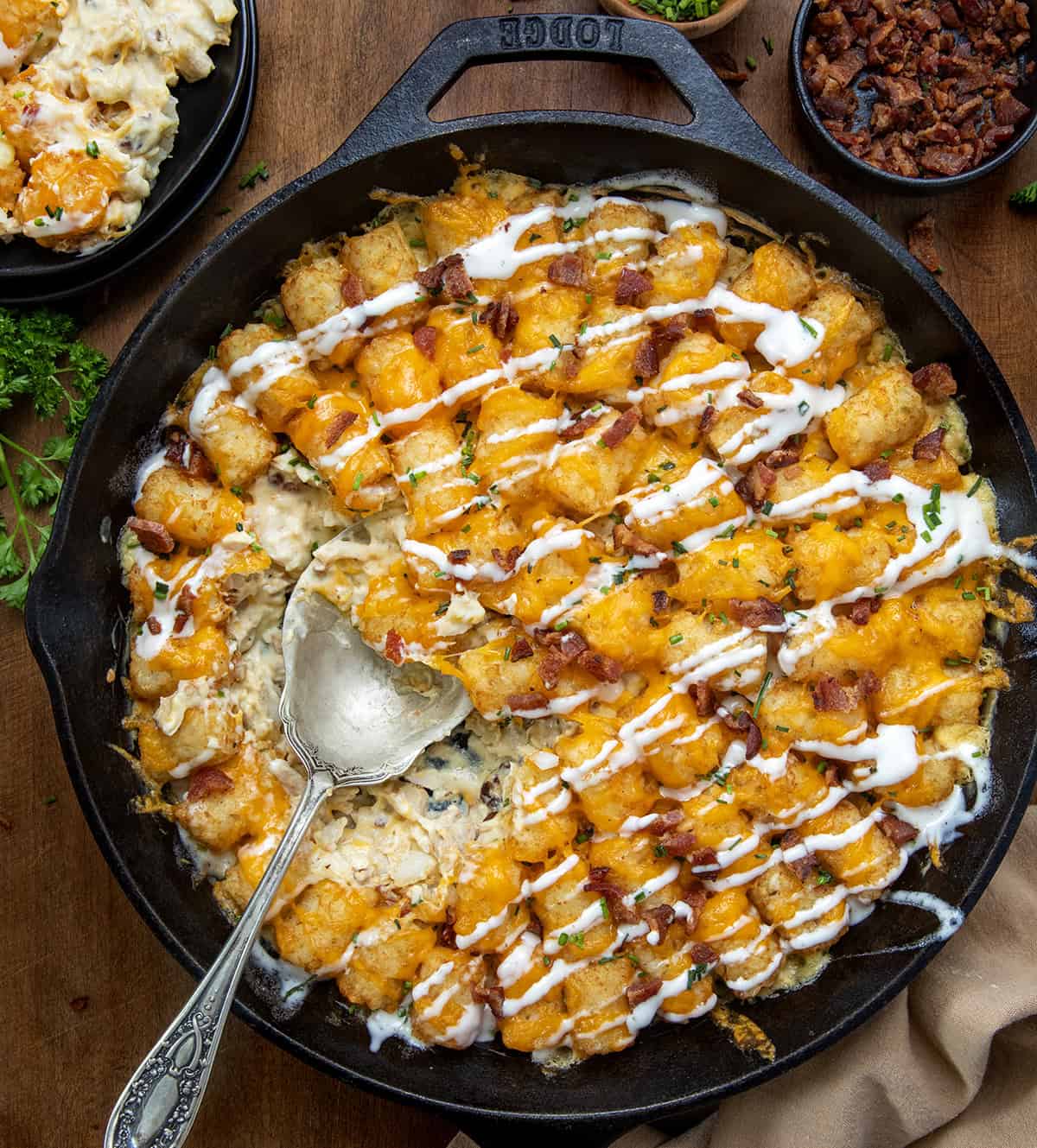 Skillet of Chicken Bacon Ranch Tater Tot Casserole with a portion missing and a spoon in the pan from overhead.