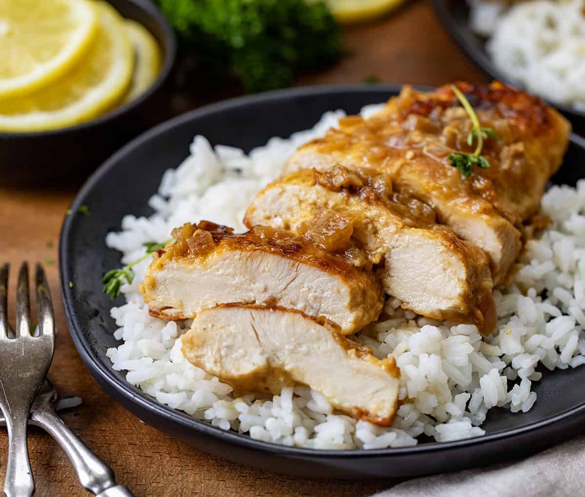 Chicken Breasts with Lemon Sliced and on a bed of rice on a black plate.