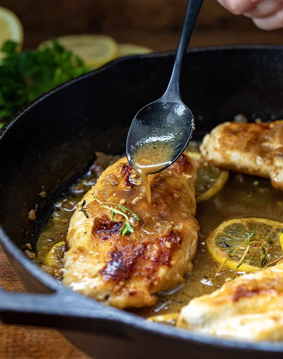 Drizzling lemon sauce over chicken breasts in a skillet.