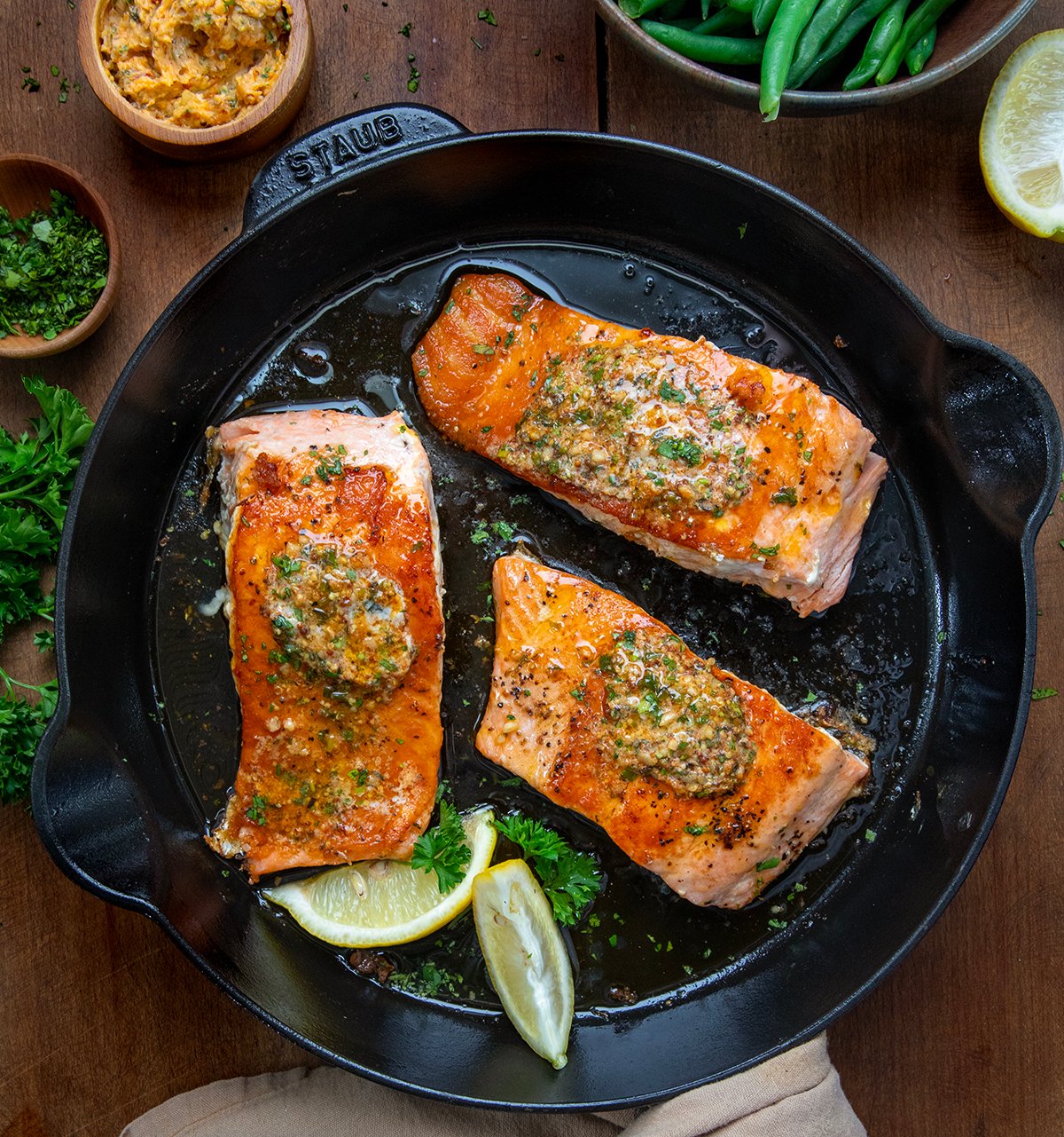 You have to try this Cowboy Butter Salmon! It is a flavorful dinner that feels restaurant-worthy, but it is ready in under 20 minutes! Cowboy Butter Salmon in a skillet on a wooden table from overhead.