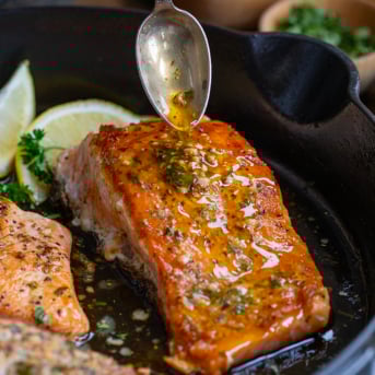 Drizzling cowboy butter over cooked salmon.