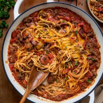 Pot of One Pot Cowboy Spaghetti on a wooden table with a wooden spoon in the pan.