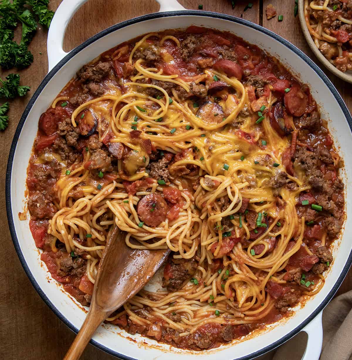 Pot of One Pot Cowboy Spaghetti on a wooden table with a wooden spoon in the pan.