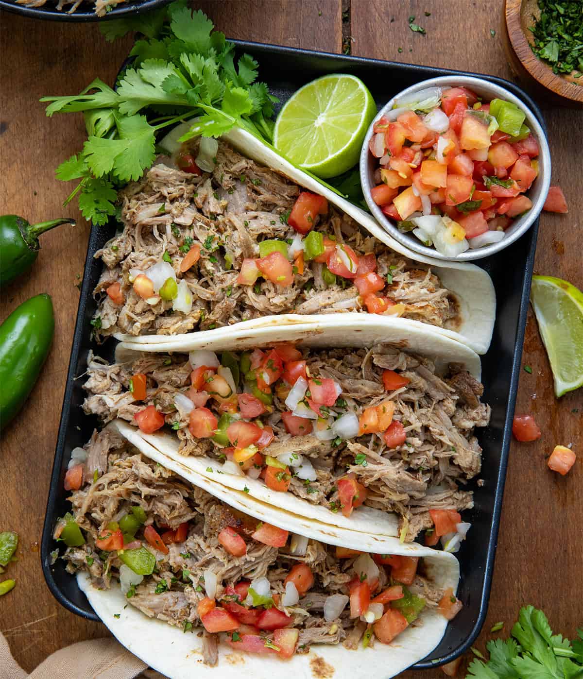 Slow Cooker Carnita tacos on a black platter from overhead.